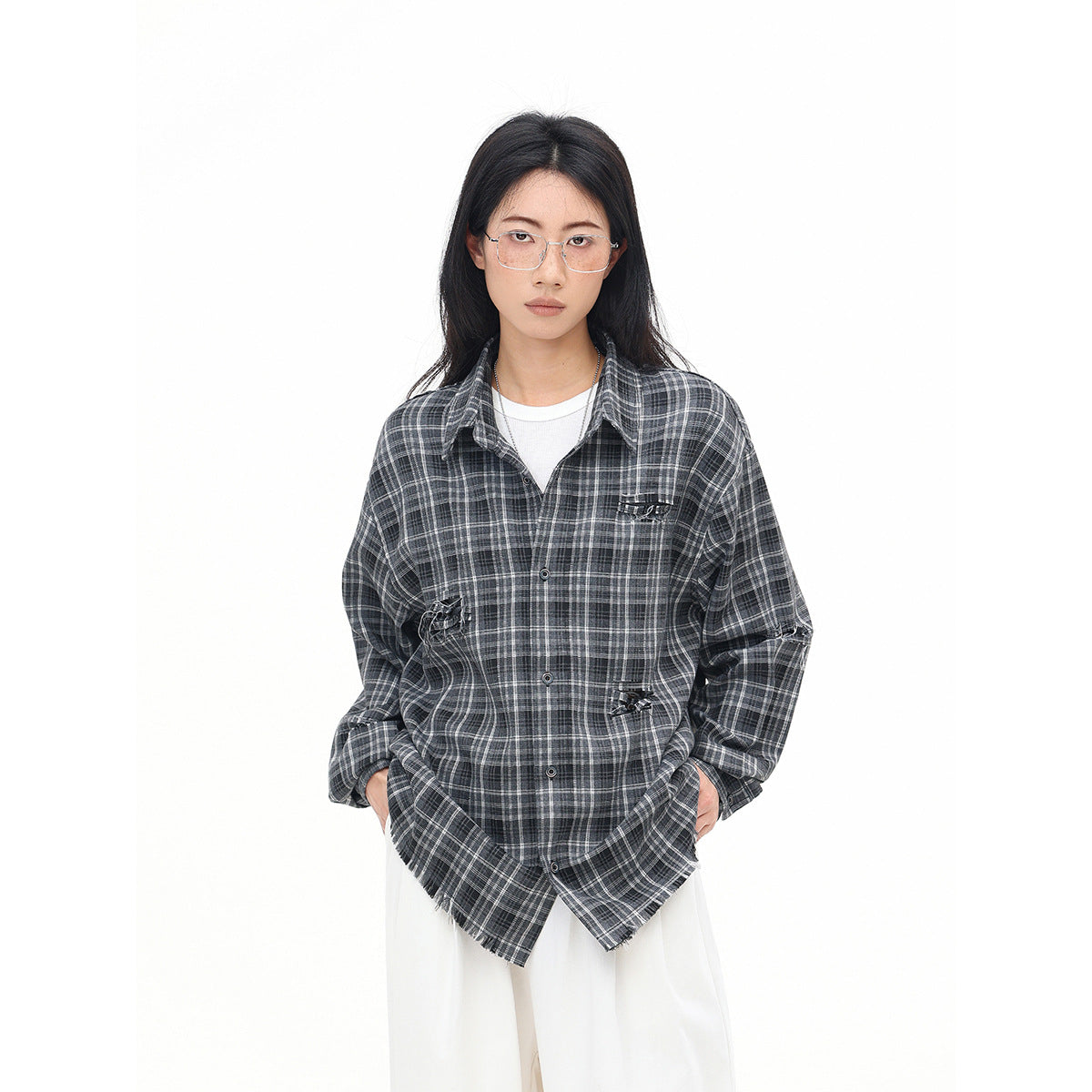 Front view of a model wearing an oversized charcoal gray plaid button-up shirt with distressed details over white trousers.