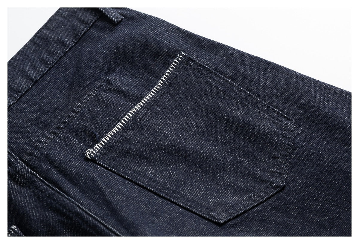 Close-up of a patch pocket with pale zigzag edge stitching on dark indigo trousers.