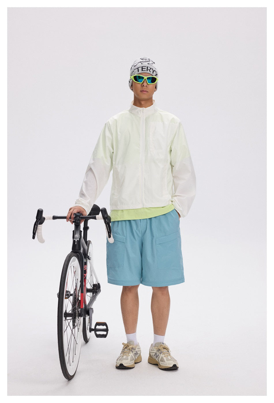 Front view of a man in a pale jacket and blue shorts standing beside a road bike.