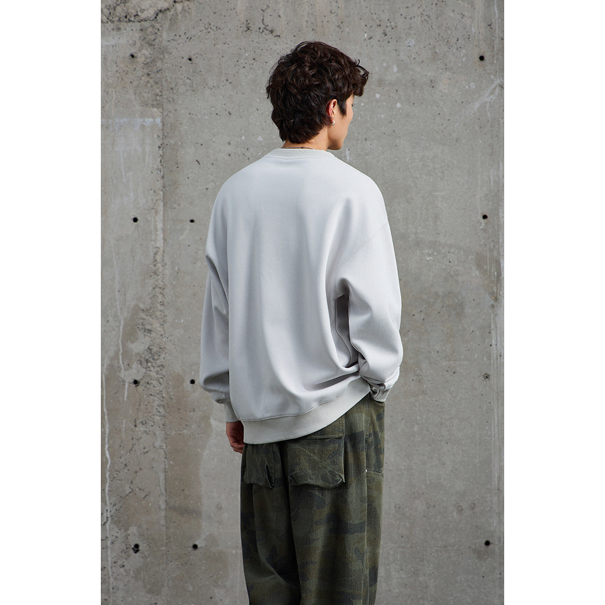 Model shown from behind wearing an oversized light gray crewneck sweatshirt with ribbed cuffs and hem.