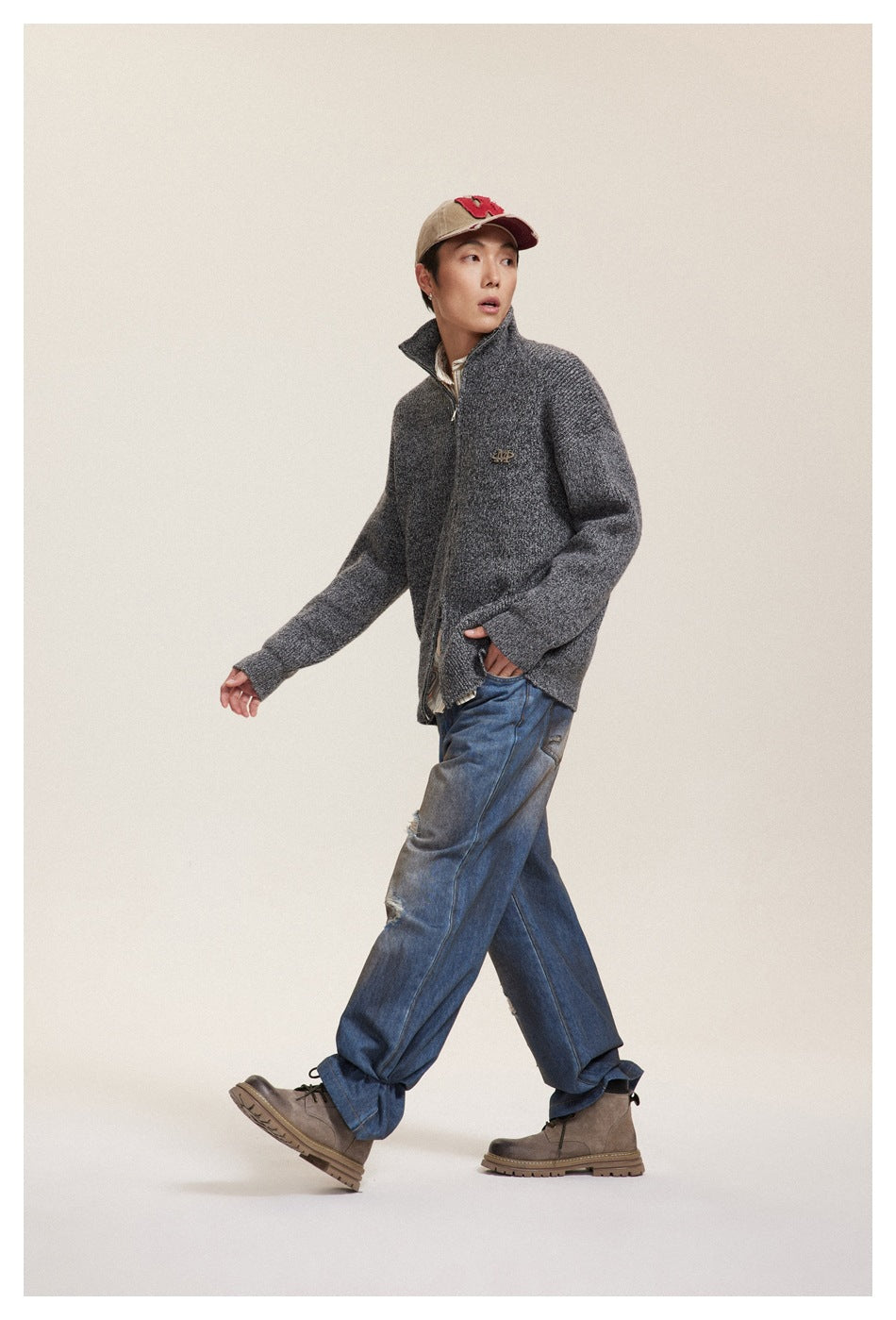 Model walking in a charcoal textured zip-up cardigan with raised collar and loose distressed blue jeans.