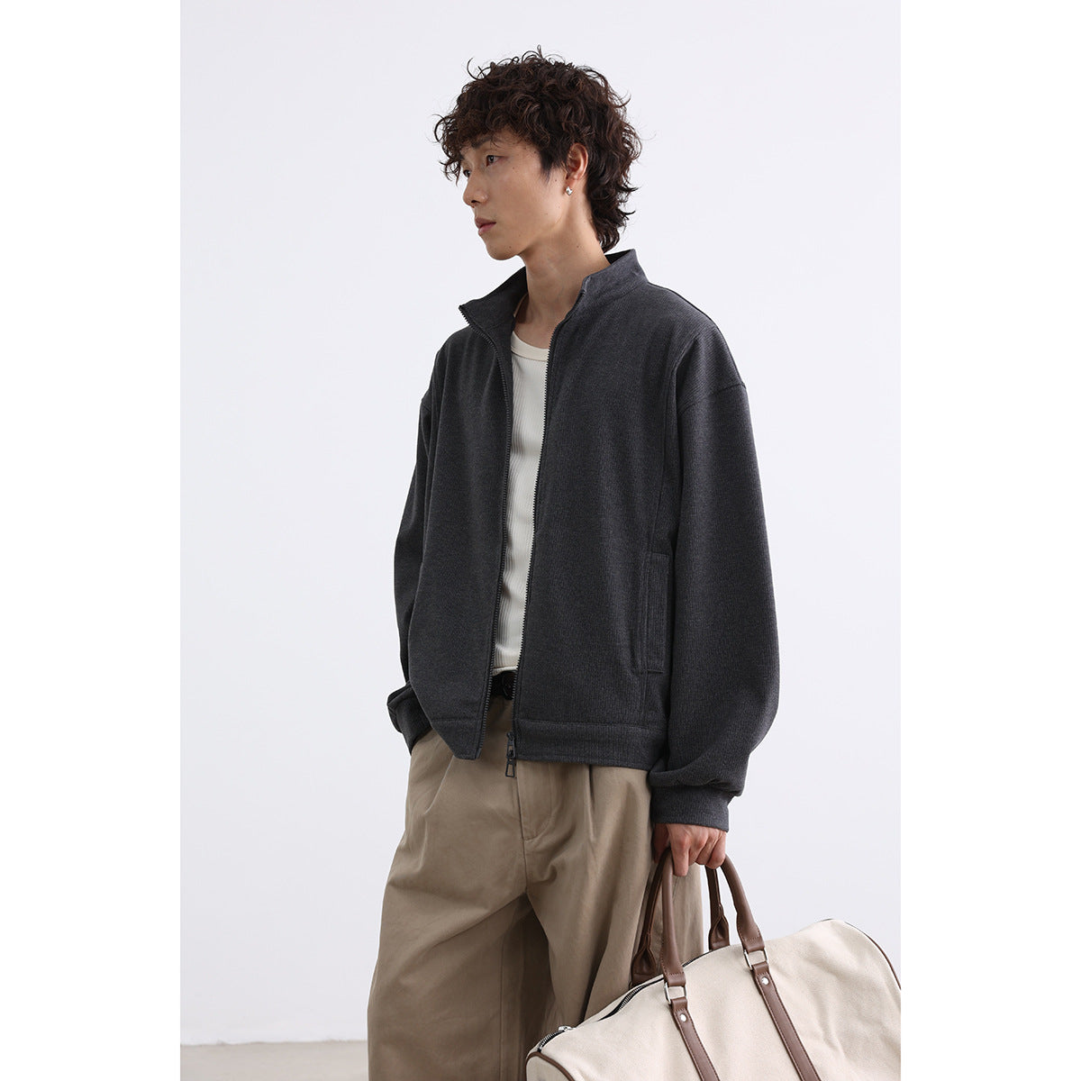 Model wearing a charcoal stand-collar zip jacket over a light top, shown at an angle.