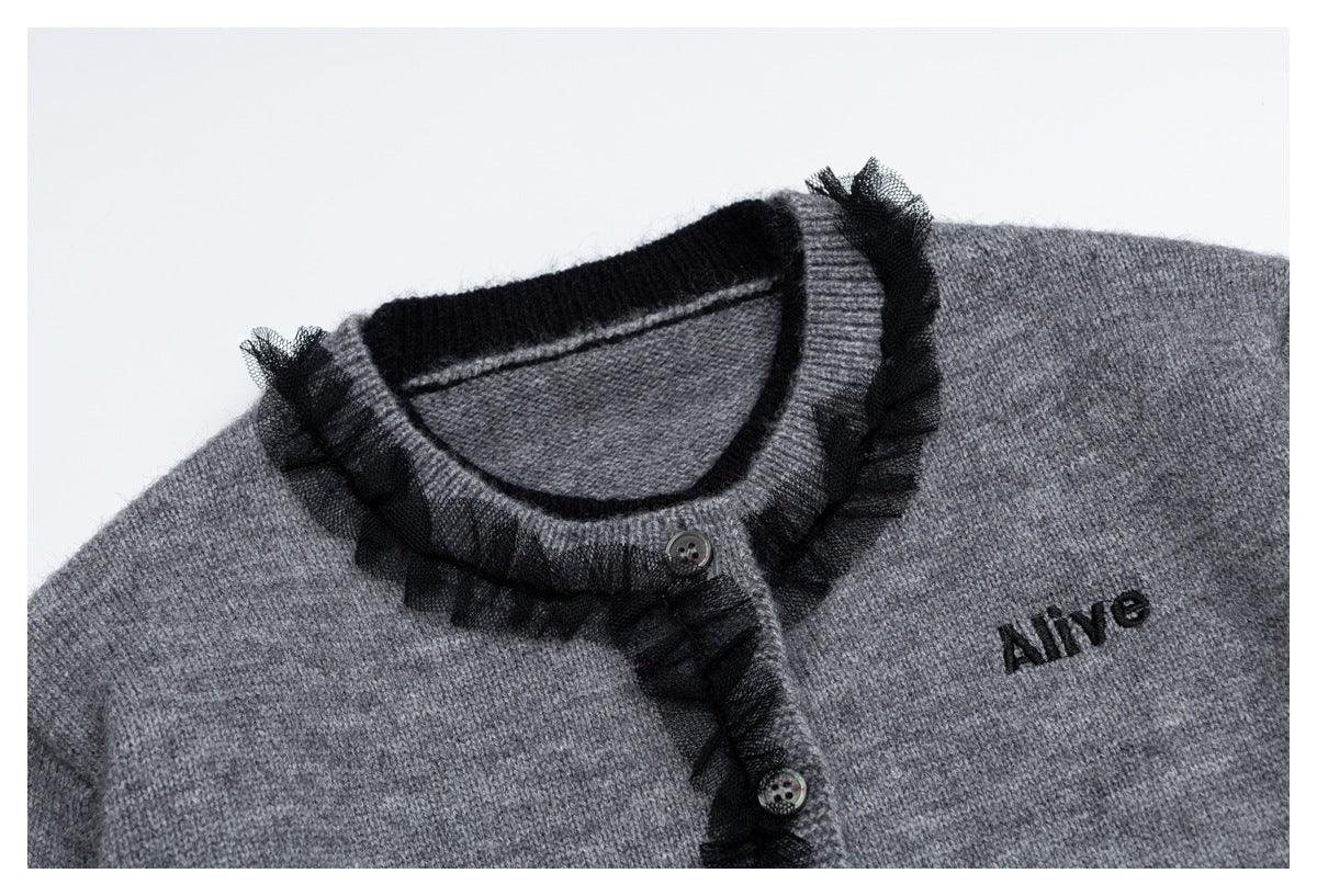 Close-up of gray cardigan neckline with black tulle ruffle trim, buttons and embroidered text