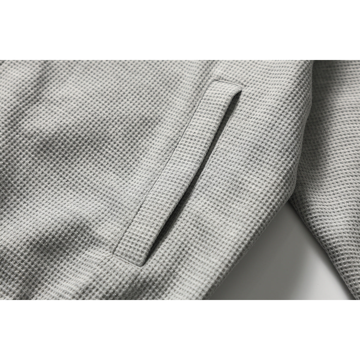 Close-up of a light gray textured jacket showing a vertical welt pocket.