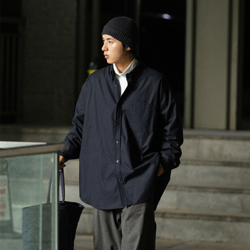 Model wearing an oversized dark navy button-up shirt over a white top, gray trousers, and a black beanie.