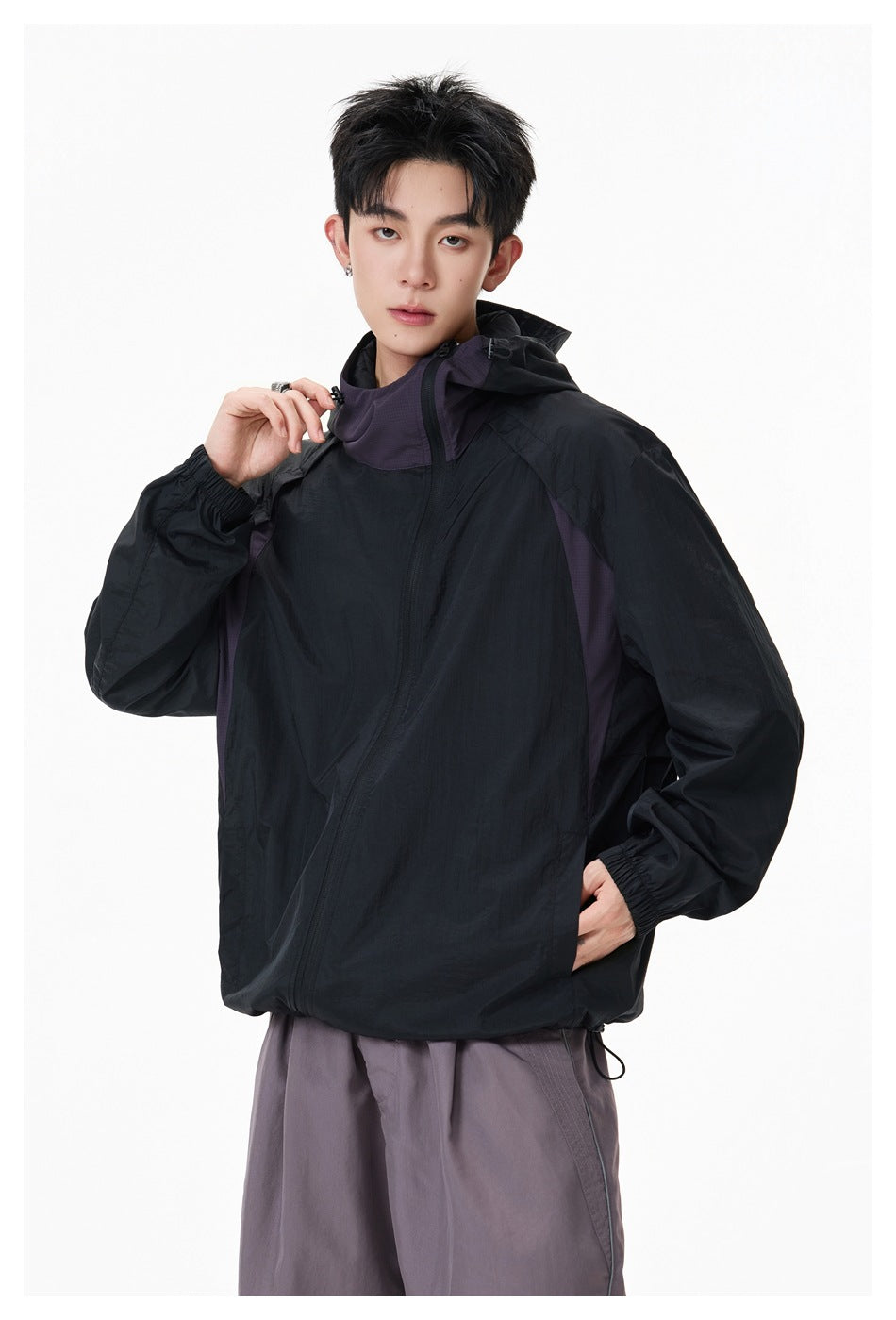 Three-quarter view of a model wearing a black hooded jacket with purple-gray panels and an angled front zipper.