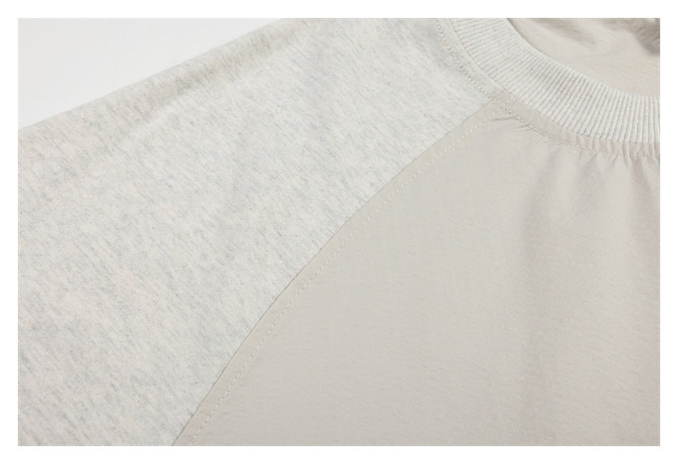 Close-up of a ribbed crew neck and raglan seam on an off-white garment with heathered sleeves.