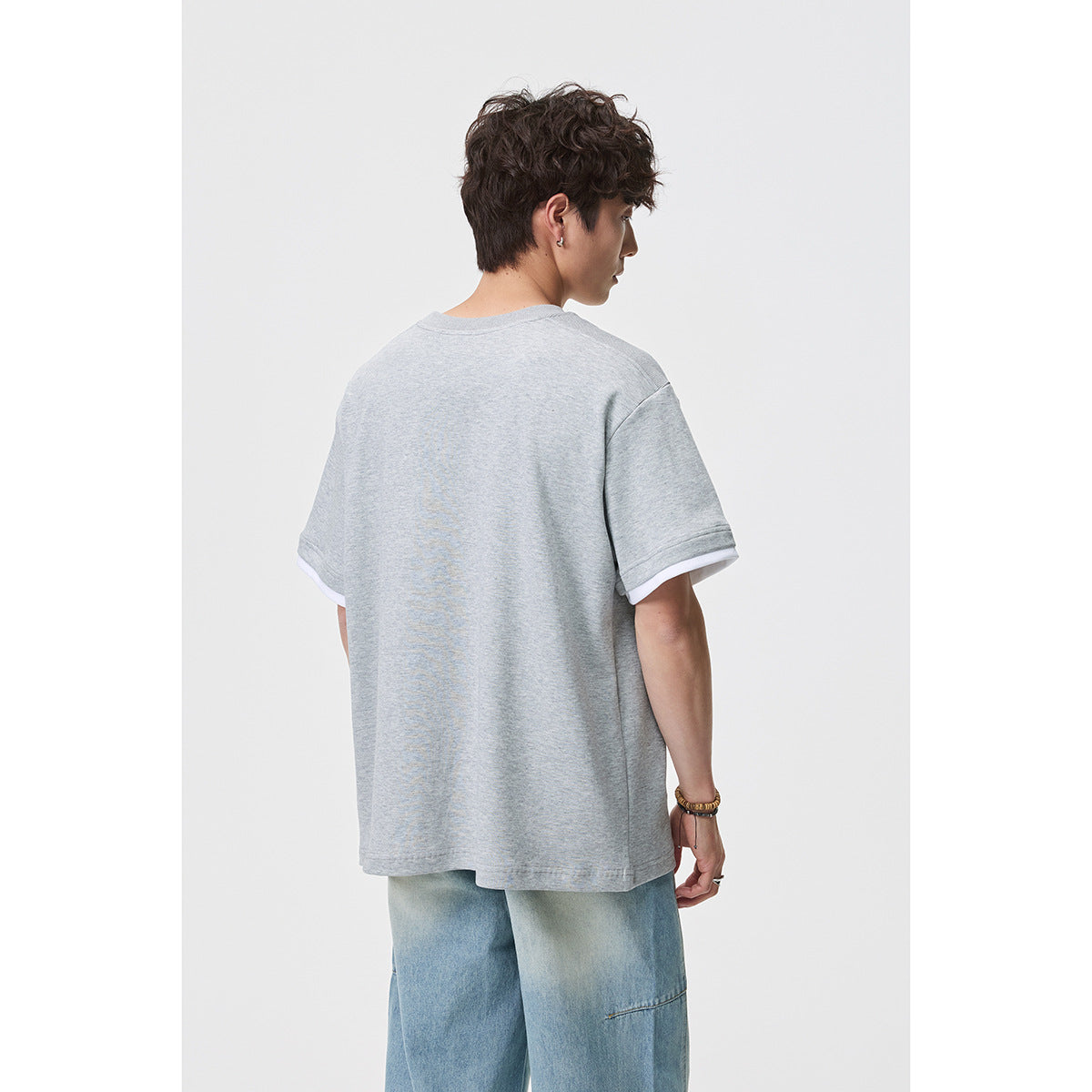 Back view of a model wearing a light gray oversized T-shirt with white sleeve layers and light blue jeans.