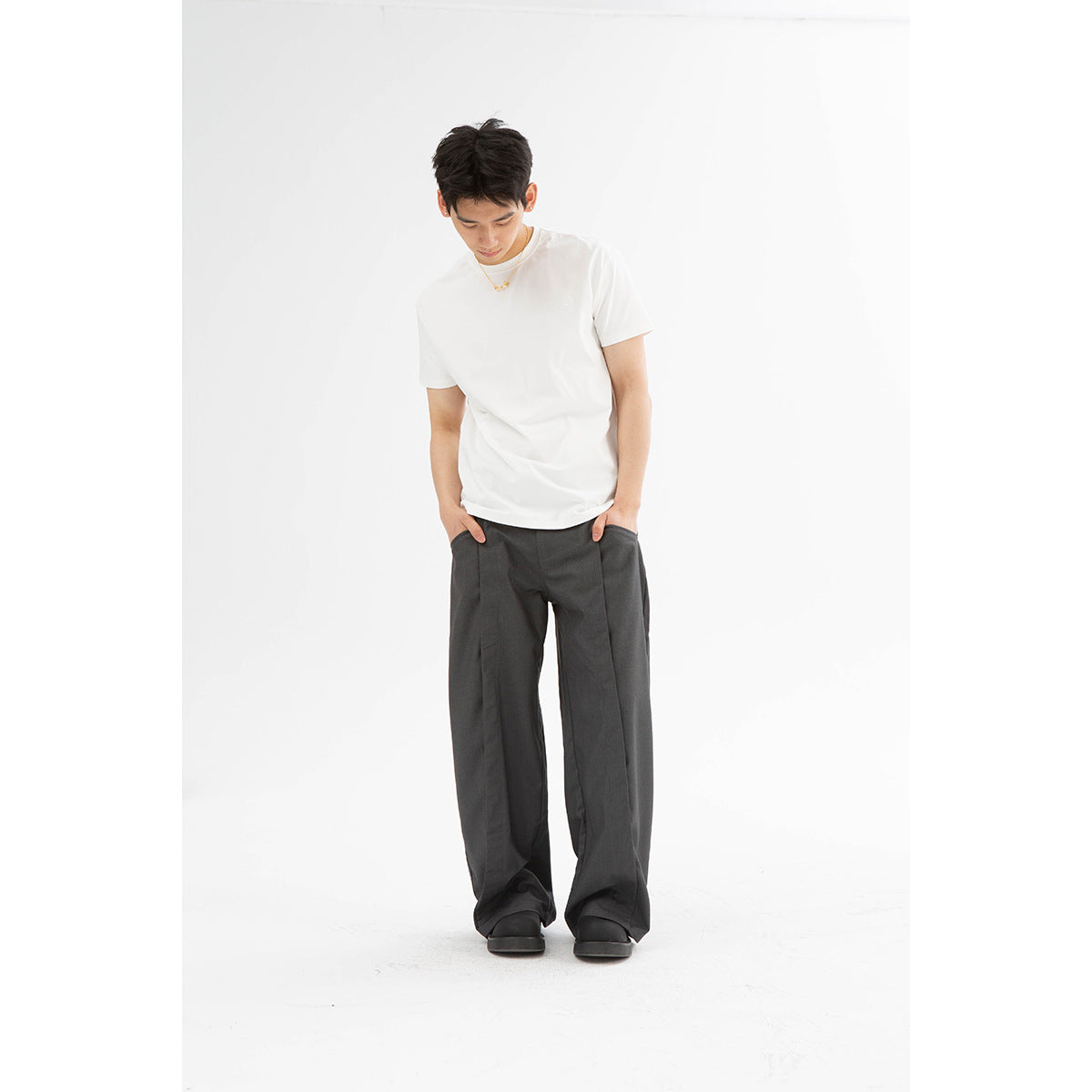 Front view of a model wearing a white T-shirt and loose charcoal-gray trousers.