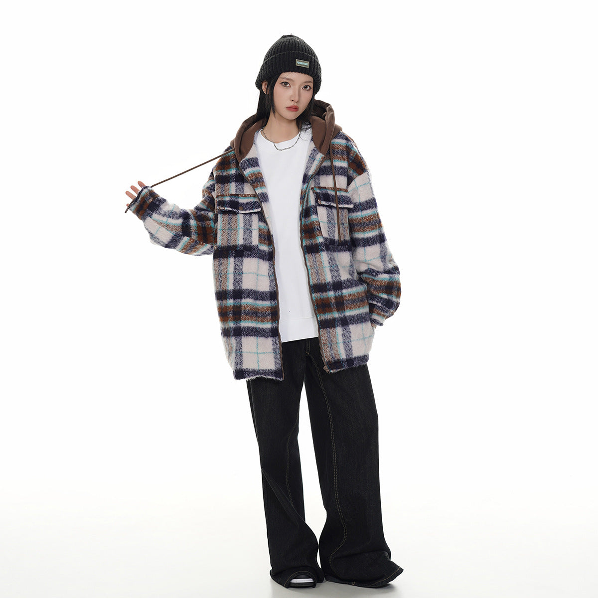 Model wearing a white, navy, teal, and brown plaid hooded jacket with black wide-leg jeans and a black beanie.