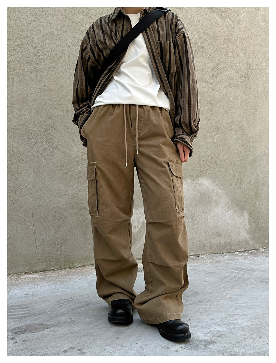Model wearing loose brown cargo pants with a drawstring waist and large thigh pockets, styled with a striped shirt.
