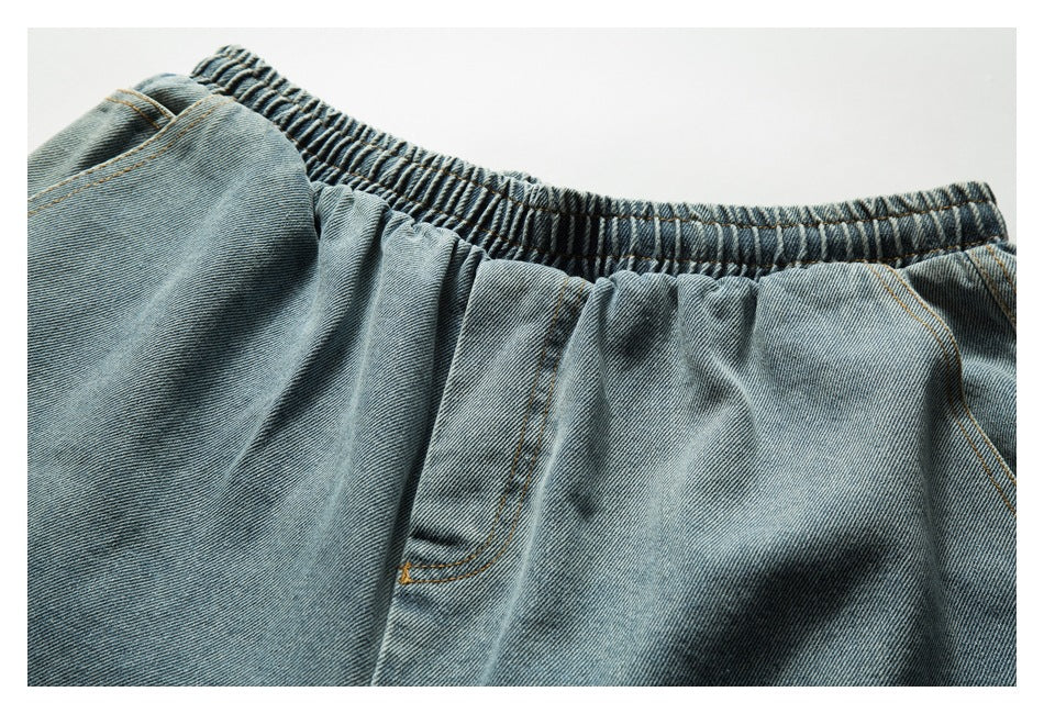 Close-up of faded blue denim shorts showing the gathered elastic waistband and front pocket opening.