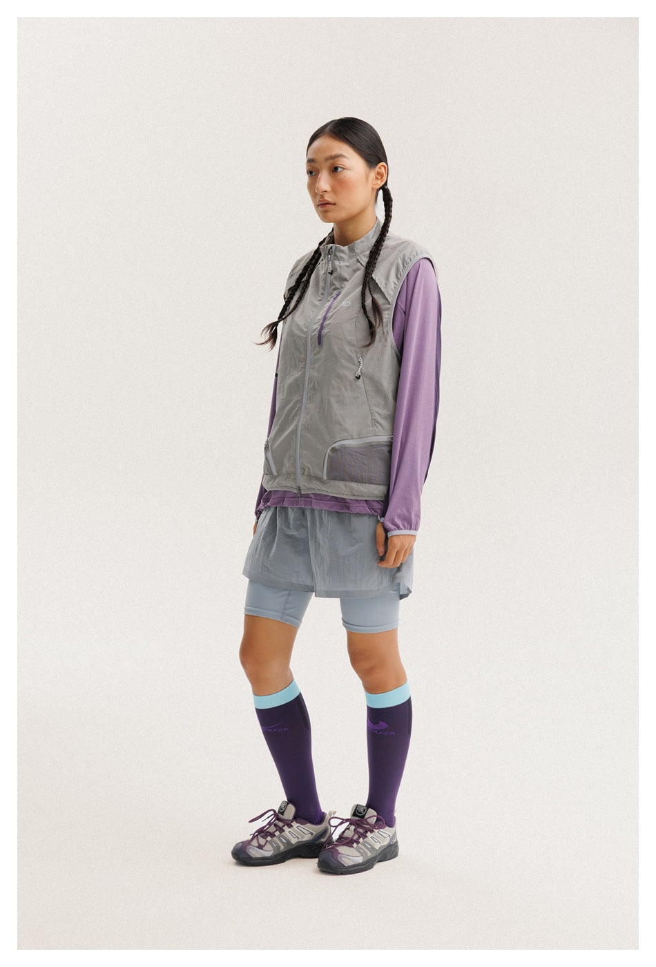 Model in a light gray zip-front vest over a purple long-sleeve top, gray shorts and purple knee-high socks.