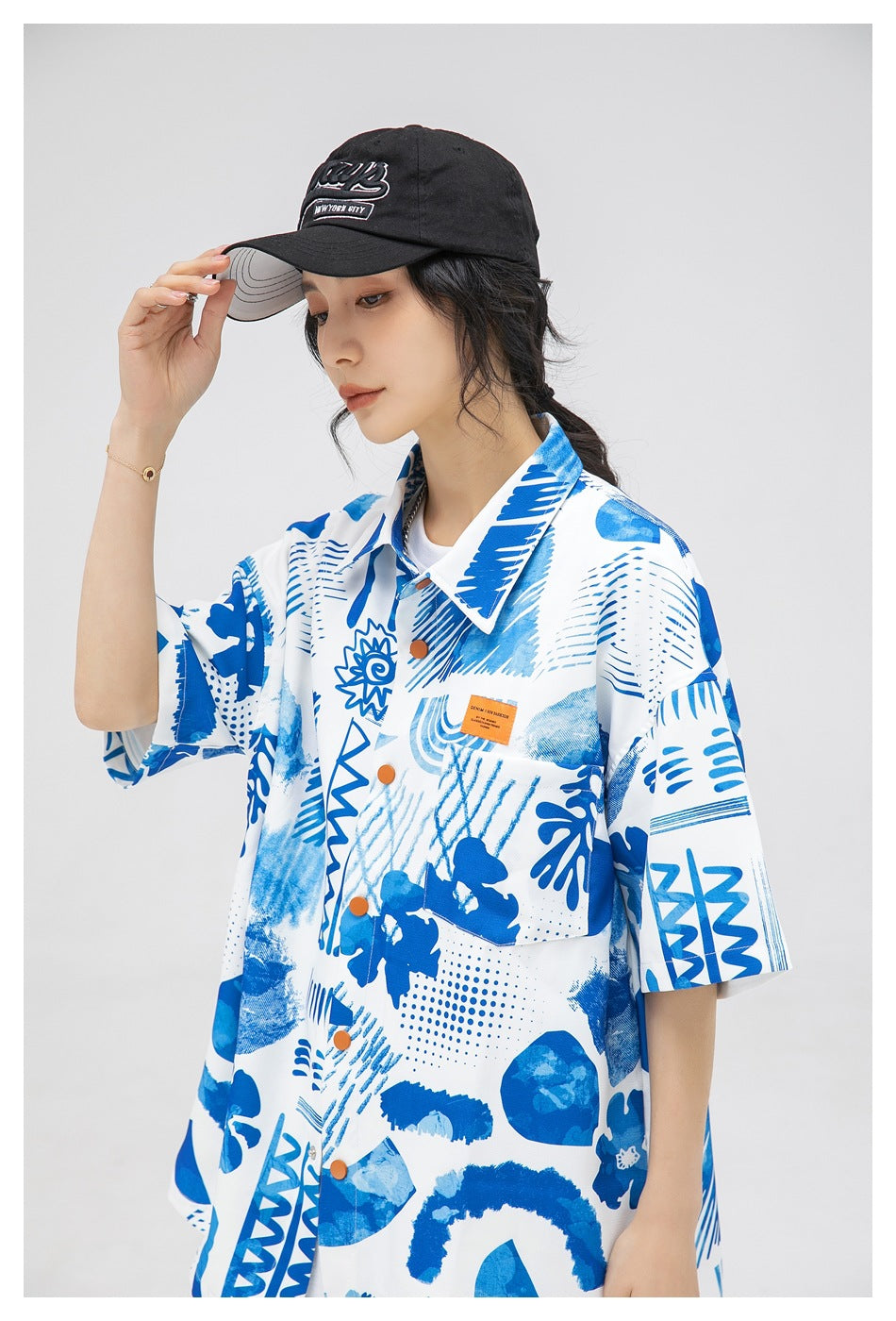 Close view of a model wearing a white shirt with blue abstract prints, orange buttons, and a chest pocket.