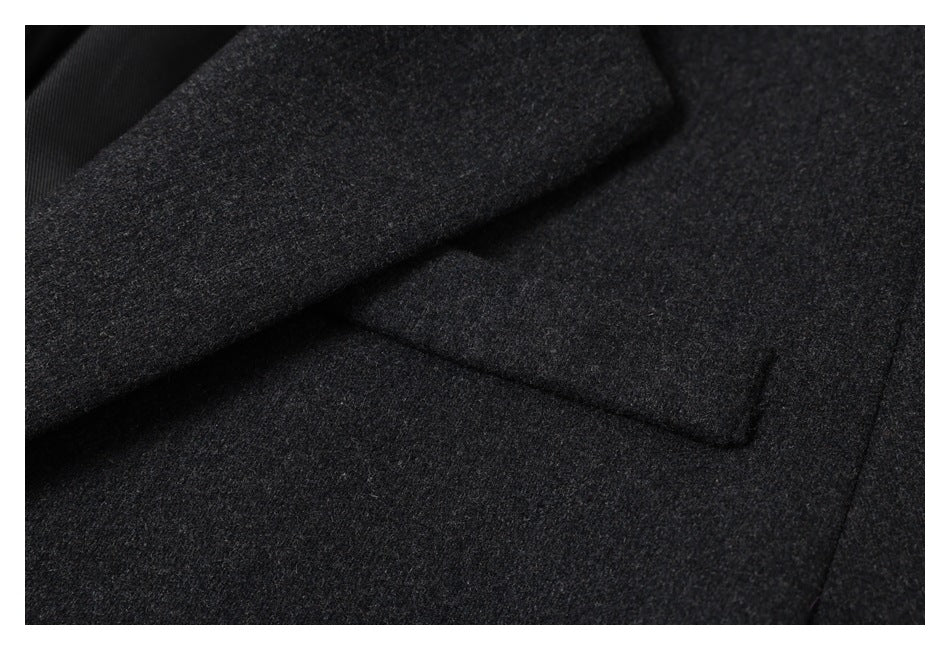 Close-up of charcoal gray coat fabric, lapel edge, and a welt pocket.