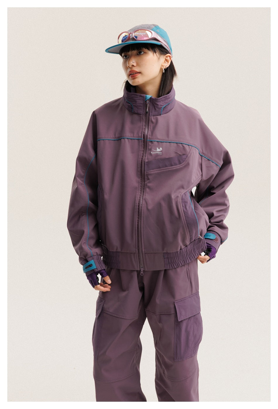 Closer view of a model wearing a plum zip jacket with turquoise piping and matching cargo pants.