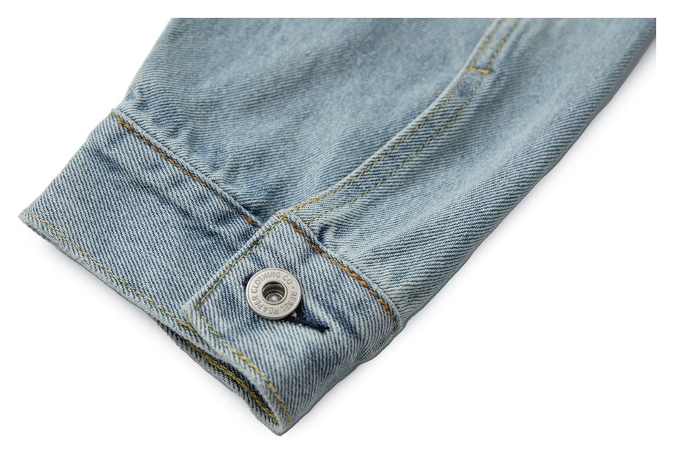 Close-up of a light blue denim jacket cuff with a silver button and tan stitching.