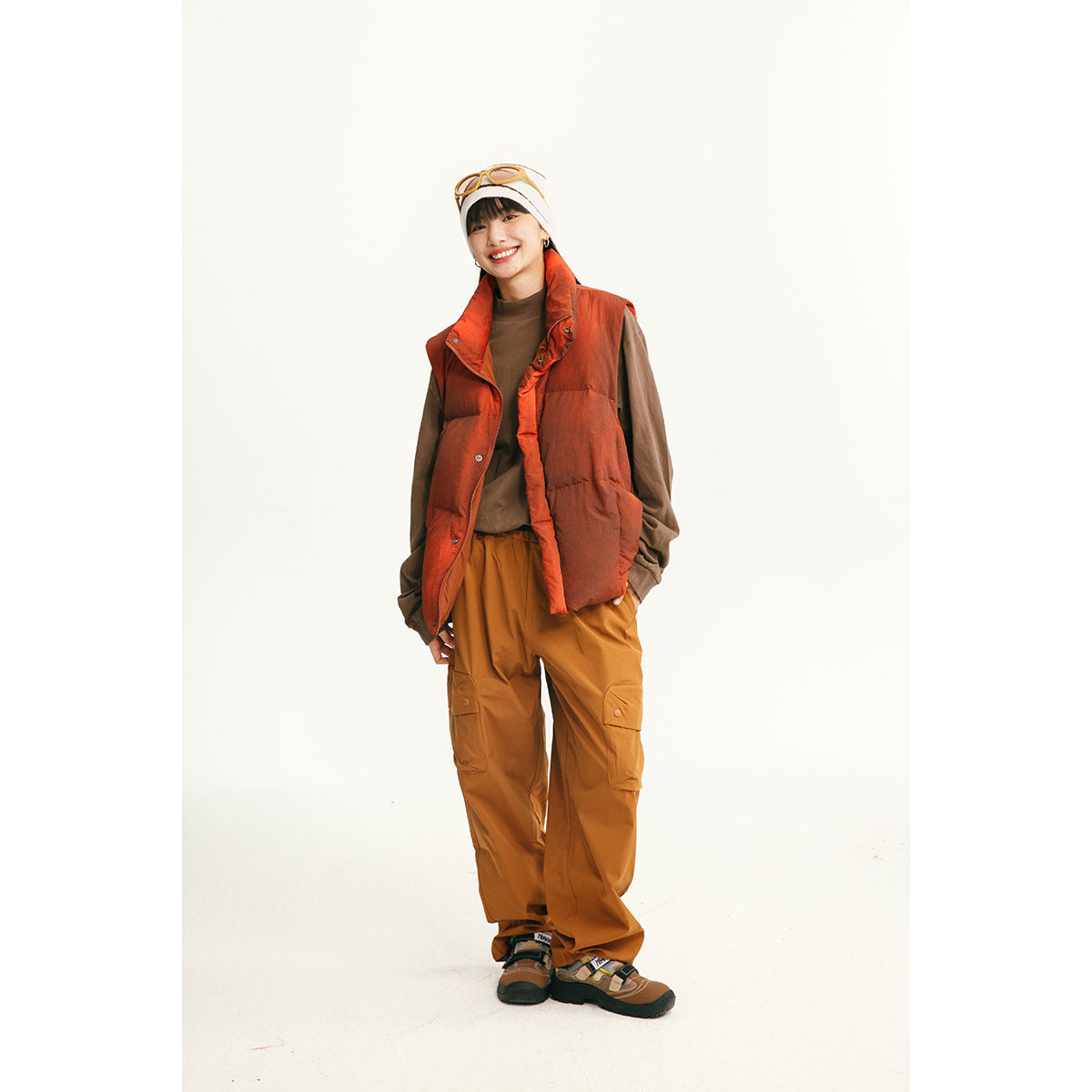 Model wearing a rust-orange quilted vest over a brown top with mustard cargo pants.