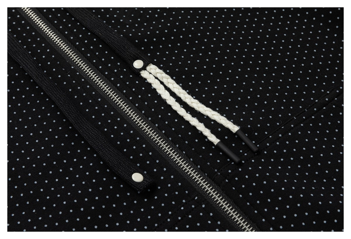 Close-up of a silver zipper, white braided drawstrings, and snap details on black dotted fabric.