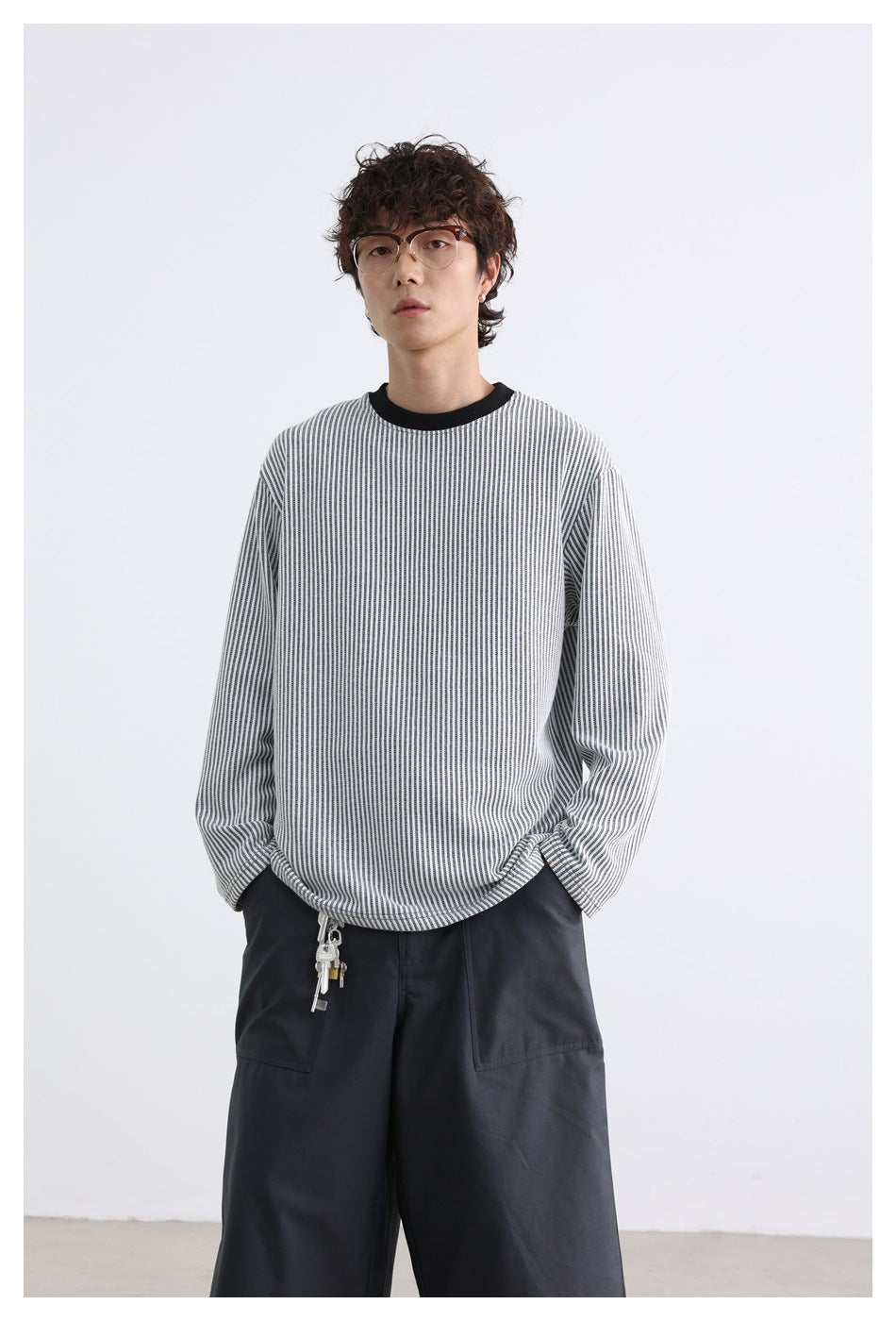 Front view of a model wearing a gray-and-white striped long-sleeve crewneck with dark trousers.