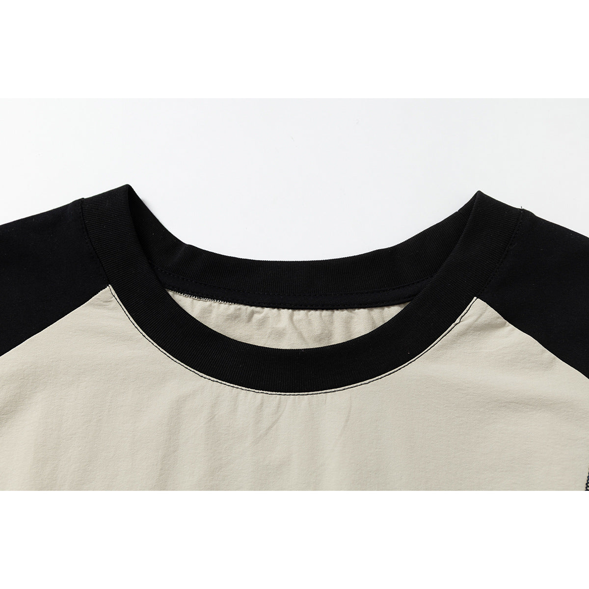 Close-up of a cream sleeveless top with a wide black ribbed crew neckline and black shoulder panels.