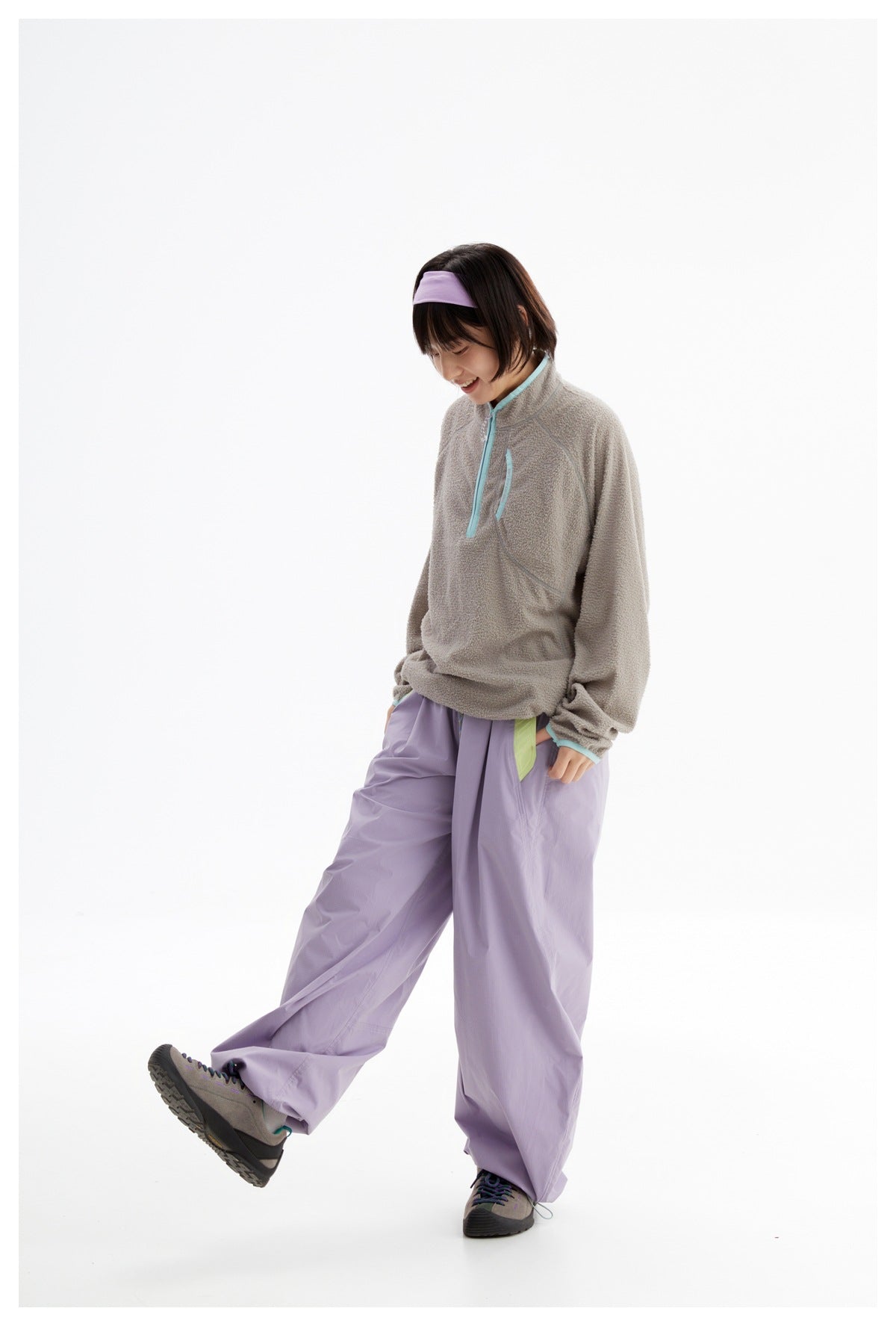 Model wearing a taupe fleece pullover with aqua trim and loose lavender pants, lifting one leg.
