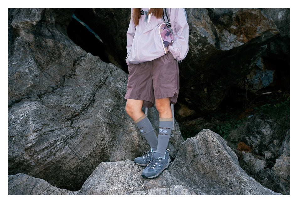 Angled front view of a hiker in mauve shorts and a pale jacket standing on rocks.