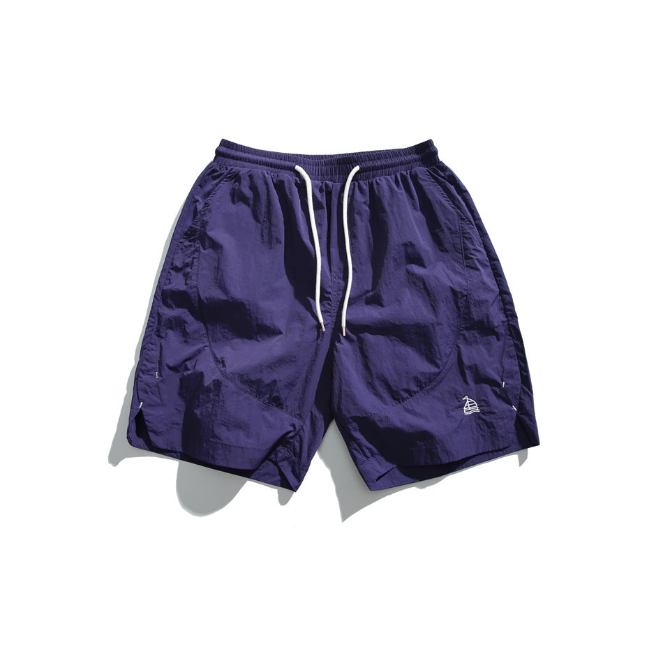 Purple knee-length shorts with elastic waist, white drawstring, and small embroidered sailboat, flat lay front view