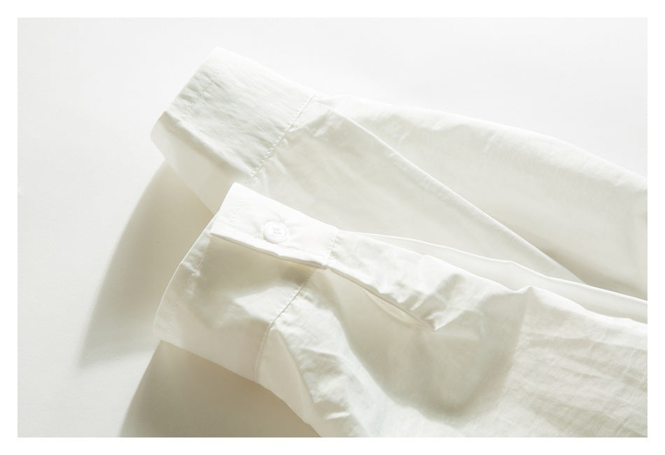 Close-up of a white garment with a small button and stitched tab beside a folded edge.