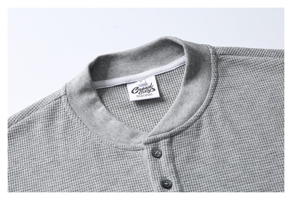 Close-up of a light gray textured henley shirt showing its collar, sewn neck label, and dark buttons.