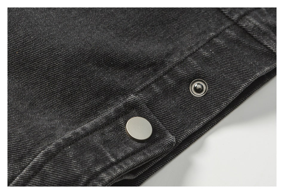 Close-up of black denim with a silver snap fastener and its socket along a stitched edge.