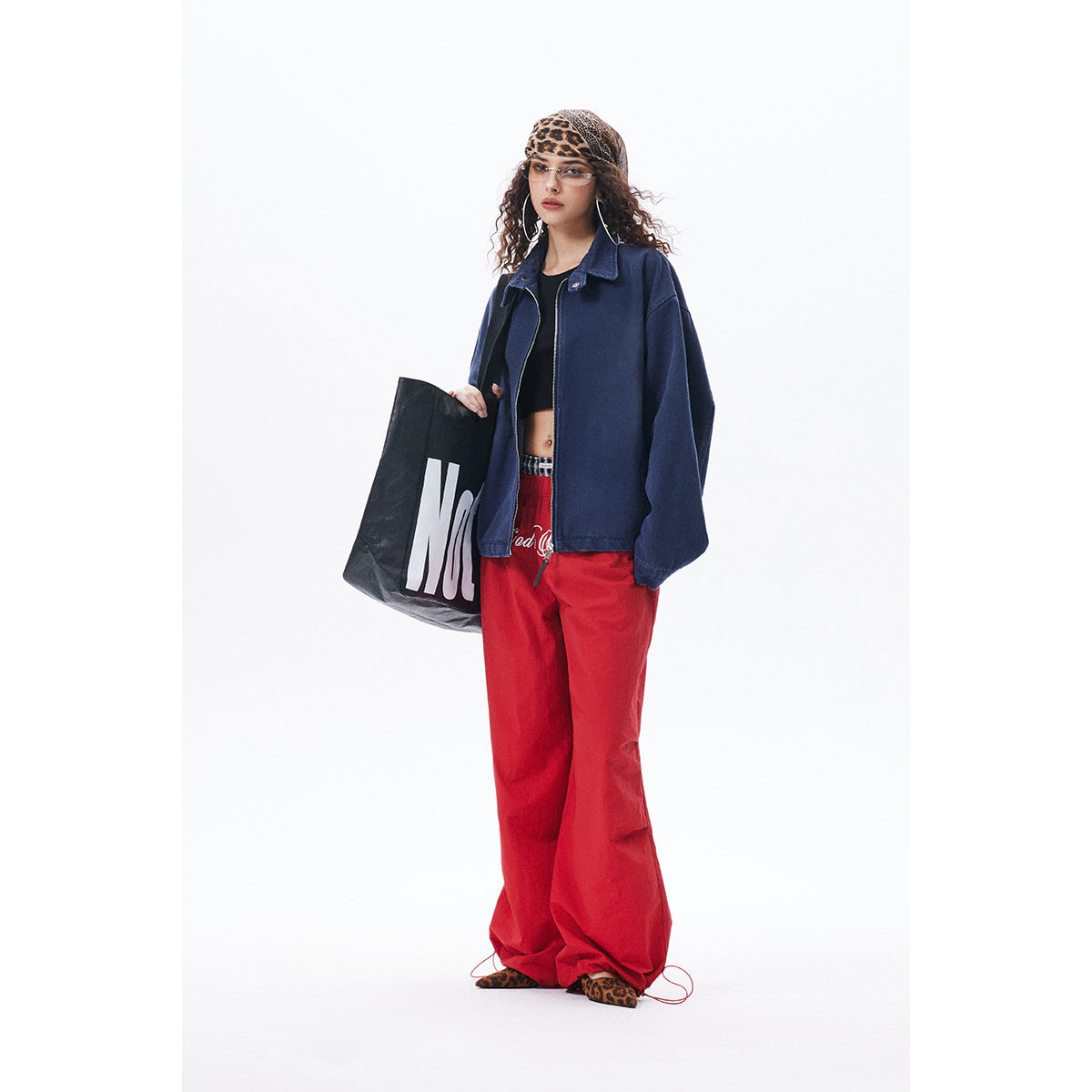 Model wearing an oversized navy zip-front jacket with a collar and wide sleeves, paired with red trousers.