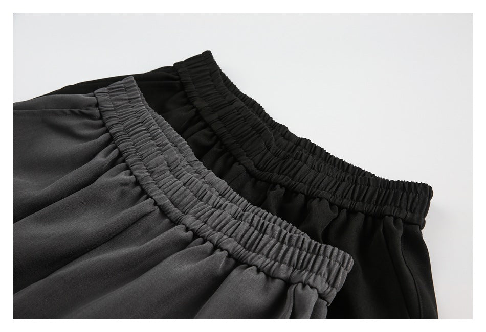 Close-up of the gathered elastic waistbands on charcoal gray and black pants.