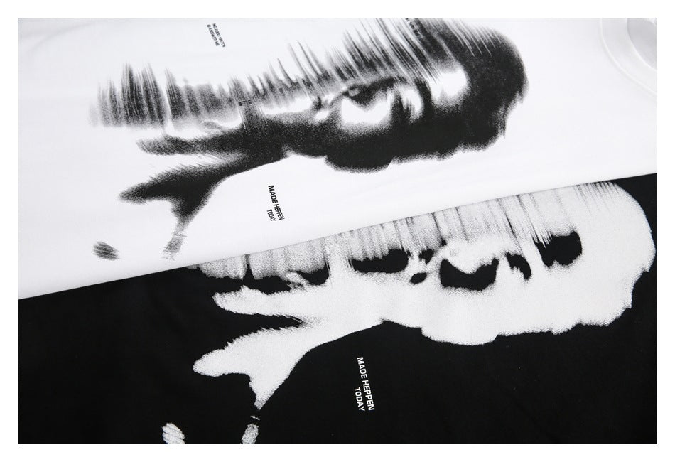 Close-up of overlapping white and black T-shirts with a large abstract black-and-white face print and small English text.