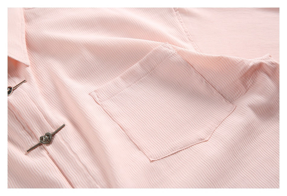 Close-up of the pale pink shirt's rectangular patch pocket and metal clasp.