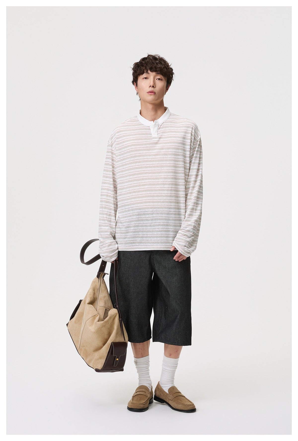 Model wearing a loose striped long-sleeve Henley top with a white collar, dark denim shorts, loafers and a tan bag