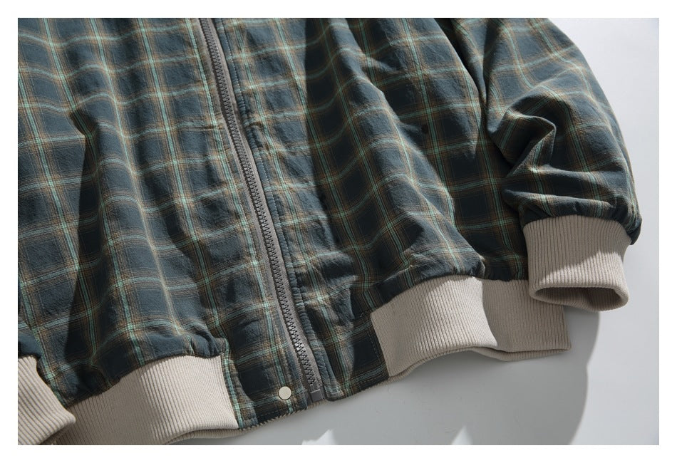 Close-up of the plaid jacket's front zipper, cream ribbed hem and cuffs, and metal snap.