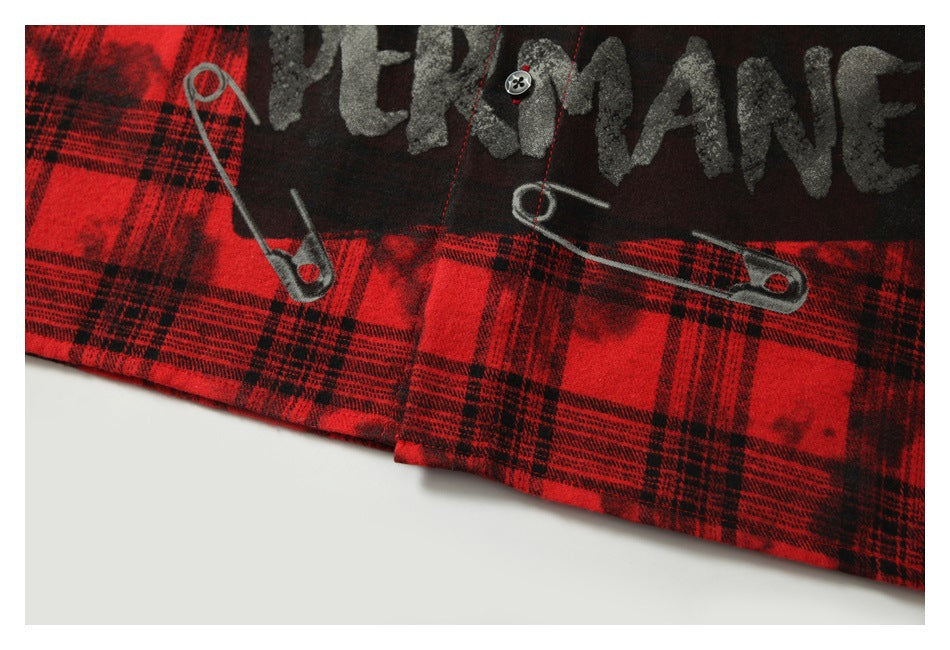 Close-up of the shirt's lower plaid hem with distressed lettering and safety-pin graphics.