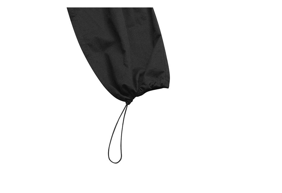 Close-up of a black pant leg hem gathered with a dangling drawcord loop.