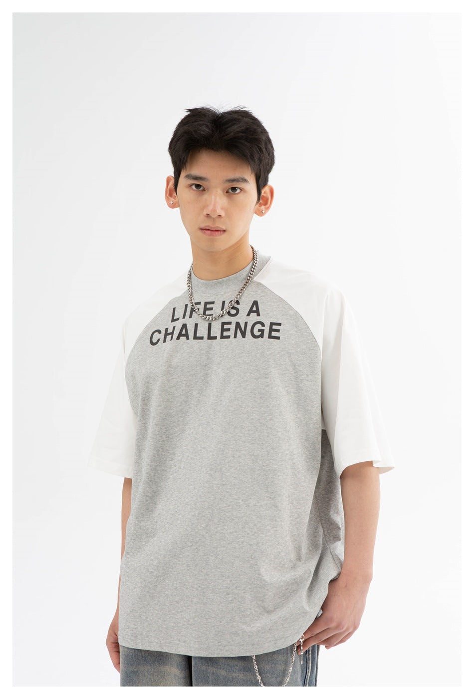 Front view of a model wearing a gray raglan T-shirt with white sleeves and bold black “LIFE IS A CHALLENGE” print.