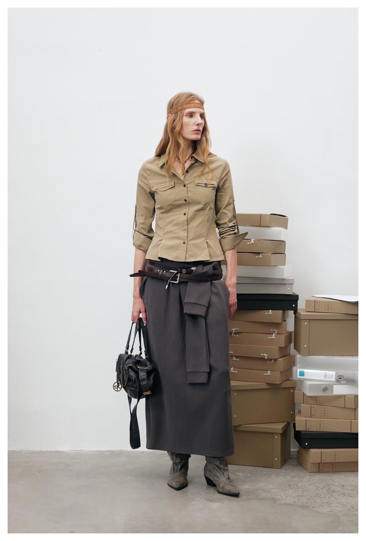 Model wearing khaki fitted shirt jacket with rolled sleeves, a dark gray skirt and a brown belt, full-length view