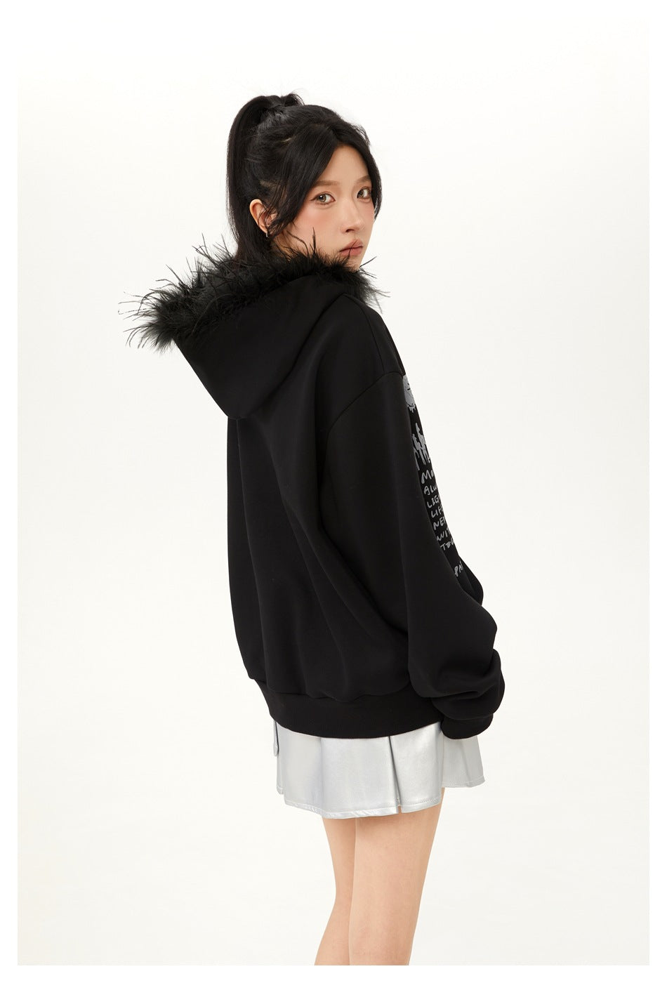 Model looking back to show the rear and side of a black oversized hoodie with fur-trimmed hood.