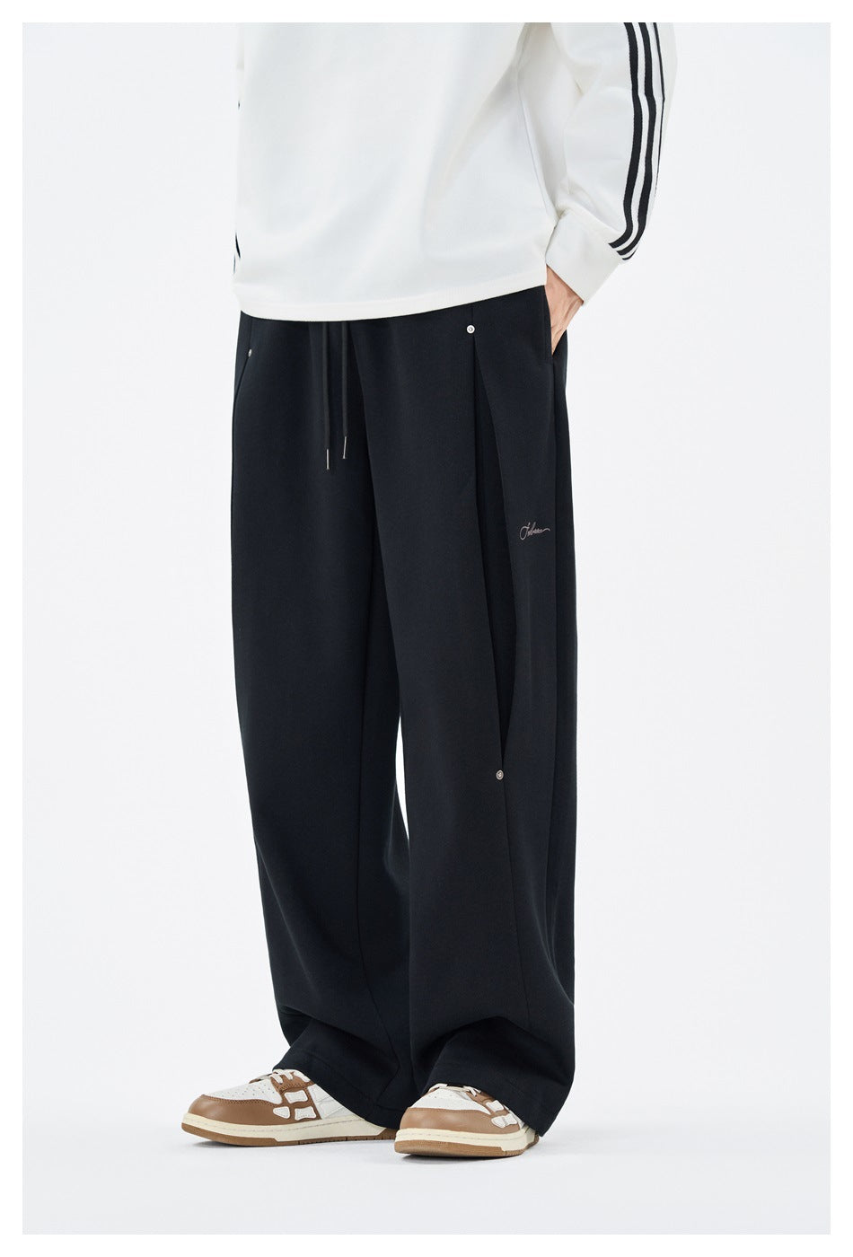 Front view of a model wearing loose black wide-leg trousers with drawstrings, pleats and a snap-button panel.