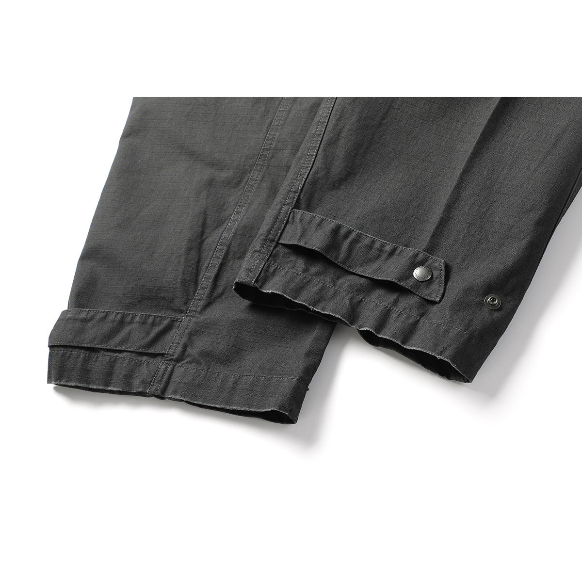 Close-up of charcoal pant hems with adjustable snap tabs and stitched panel details.