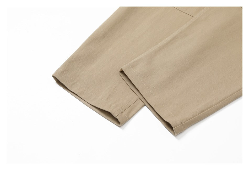Close-up of the stitched hems of beige pants against a white background.