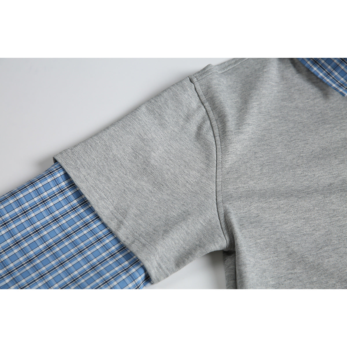 Close-up of a heather gray polo sleeve layered over a blue plaid long sleeve.