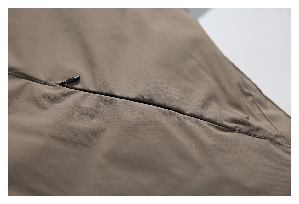 Close-up of a black zipper pull on a horizontal seam in taupe garment fabric.