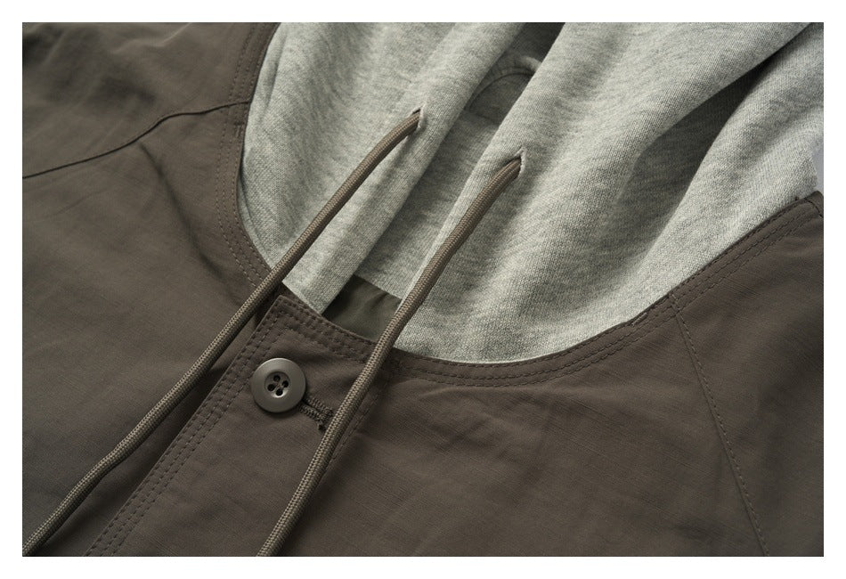 Close-up of a dark olive-brown garment with a gray knit hood, long drawcords, and a buttoned front.