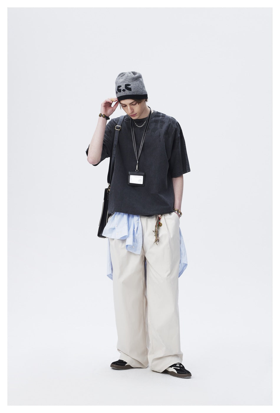 Full-length model wearing an oversized charcoal T-shirt with subtle tonal shoulder graphics and loose cream trousers.