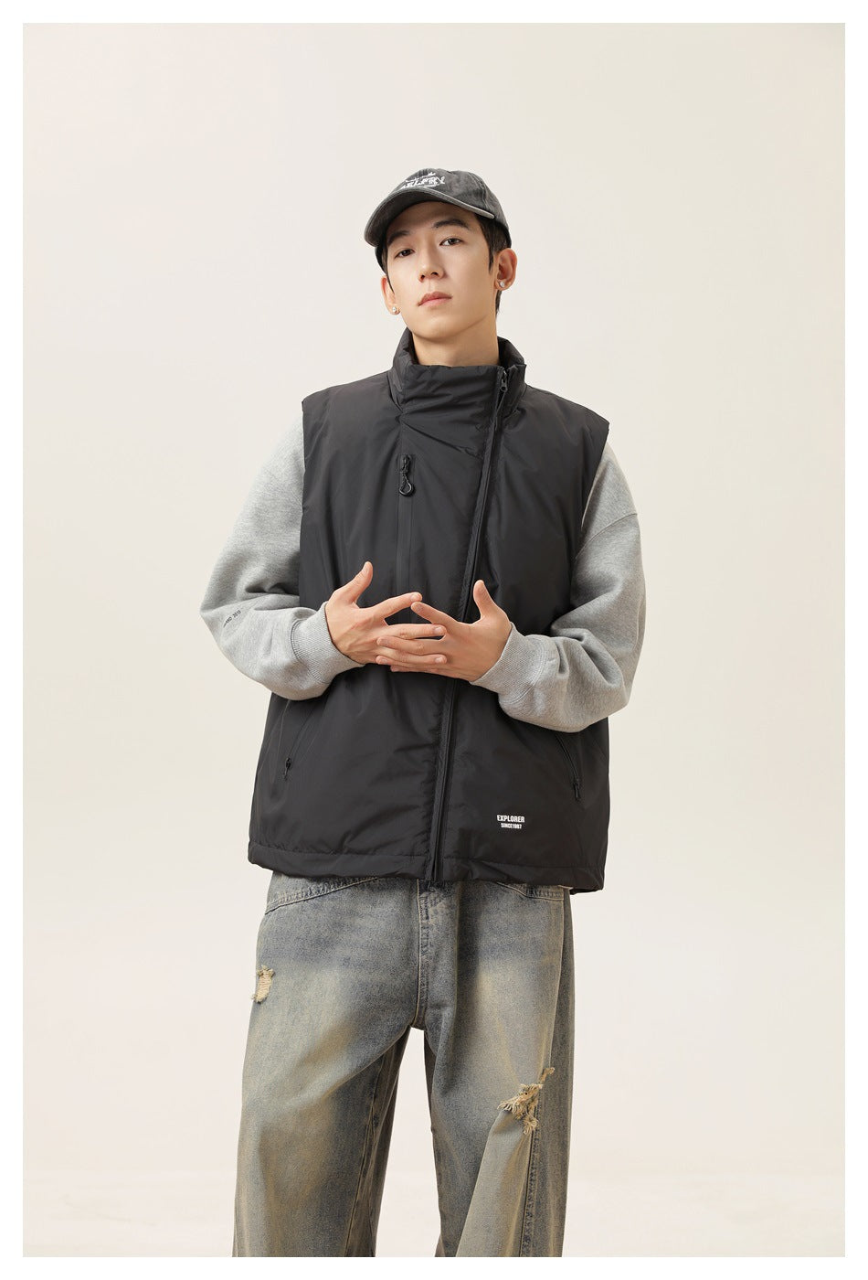 Front view of a model wearing a black high-collar zip vest over a gray sweatshirt.